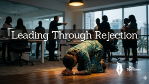 A female leader on her knees, forehead bowed low to the ground in prayer. Around her, the faint silhouettes of jeering accusers, male and female are visible but out of focus. 2 or 3 accusers are pointing at the leader. The leader is sharp and clear — this is the moment of greatest strength, not weakness. Warm intimate light from above. Cinematic, photorealistic, contemplative. The posture of surrender that becomes the posture of power. Not in a religious setting. It may be an open office. Context is Nigerian.